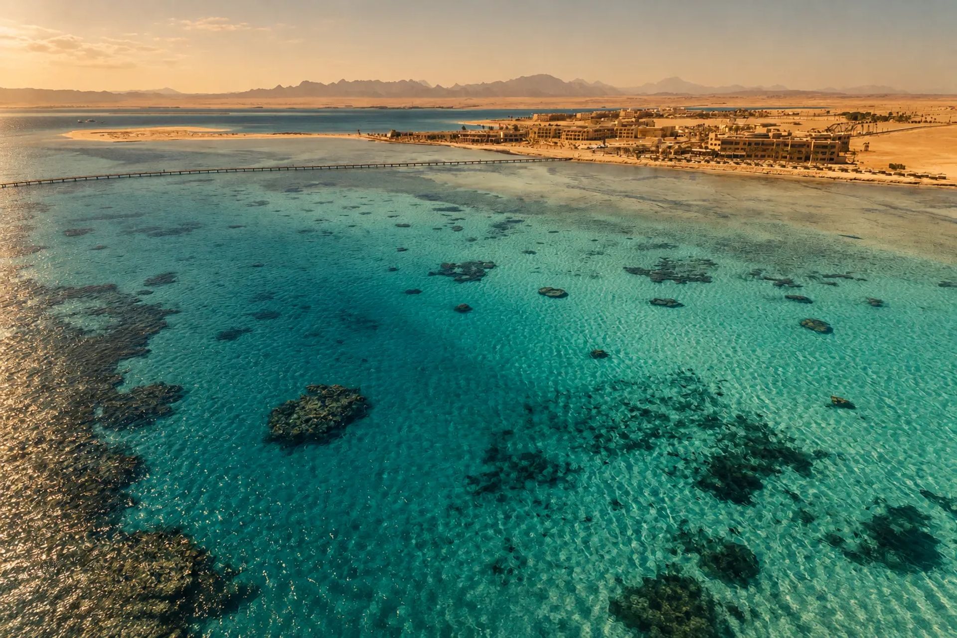Aerial view of the Soma Bay shallows, a long jetty crossing turquoise water dotted with coral heads