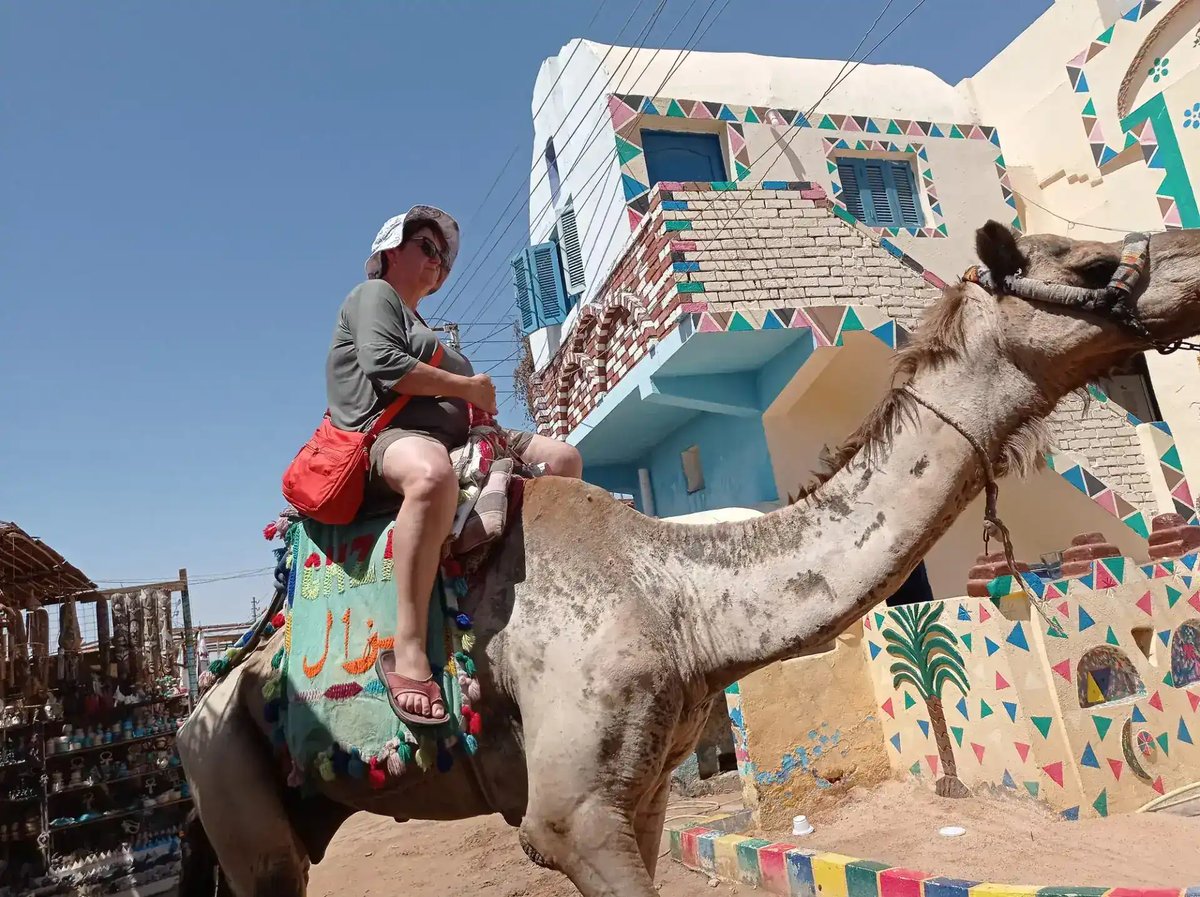 Tourist riding a camel past painted houses in a Nubian village, Aswan