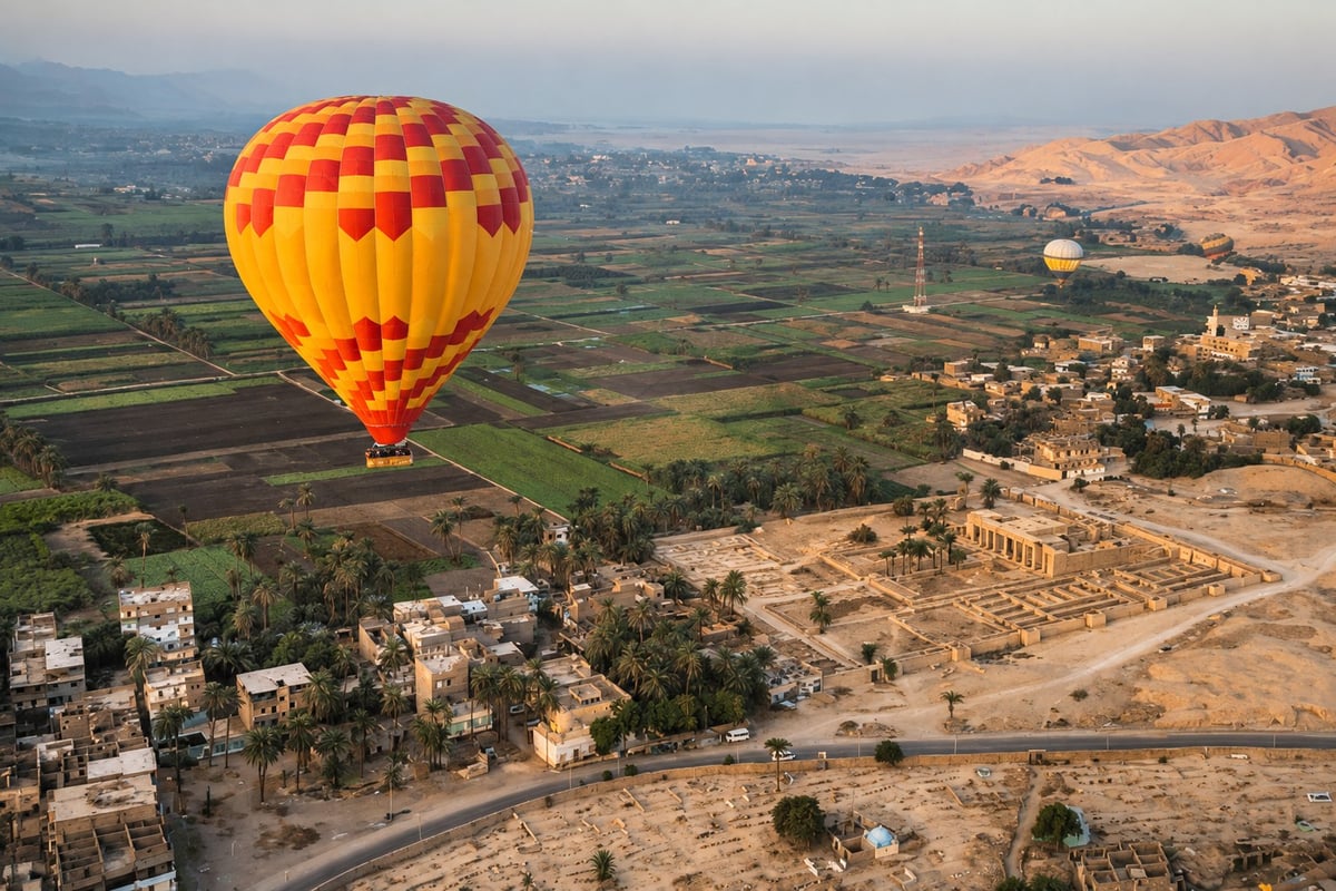 Hot air balloon at sunrise above Luxor West Bank, passing over Nile-side fields and visible ancient ruins