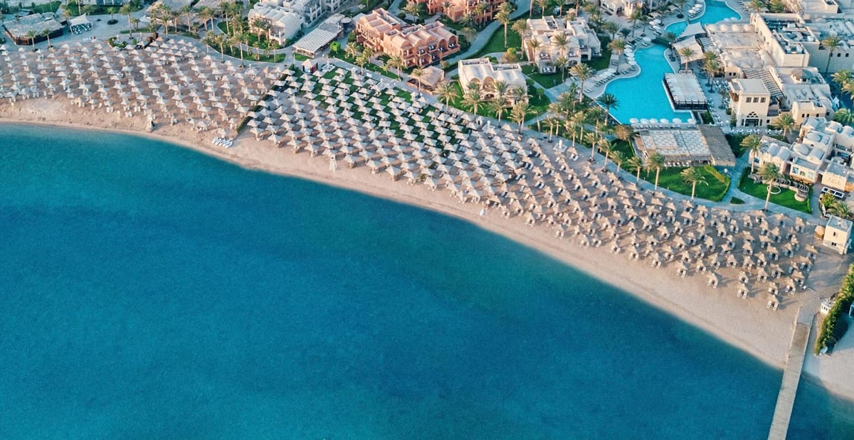 JAZ Makadina beach with rows of shade umbrellas and a curved shoreline.