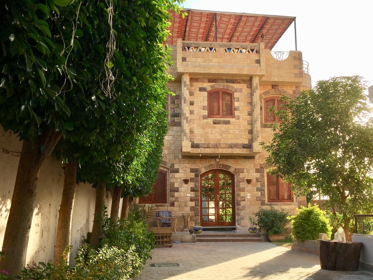 New Memnon Hotel Luxor entrance courtyard with a stone façade and leafy trees.