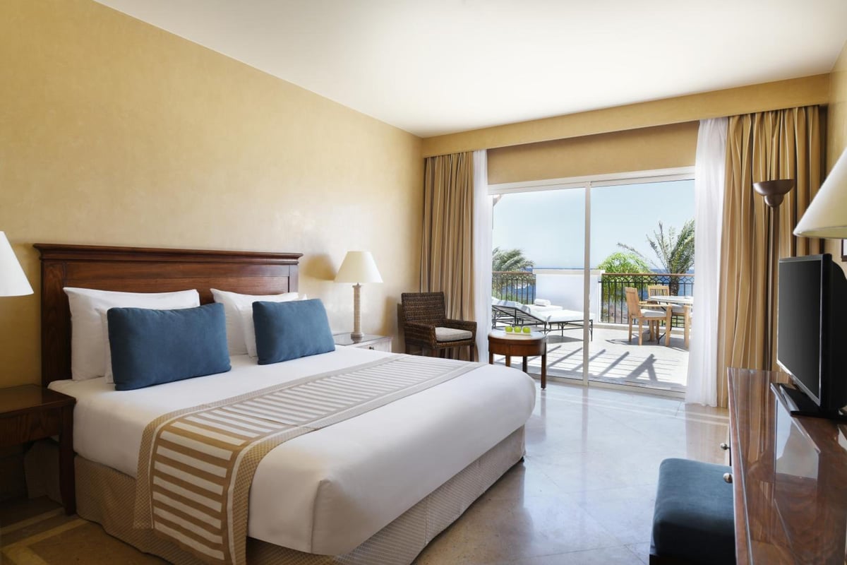 JAZ Dahabeya guest room with a large bed and sliding glass doors.
