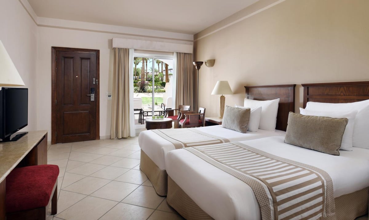 JAZ Dahabeya twin bedroom with two beds and glass balcony doors.