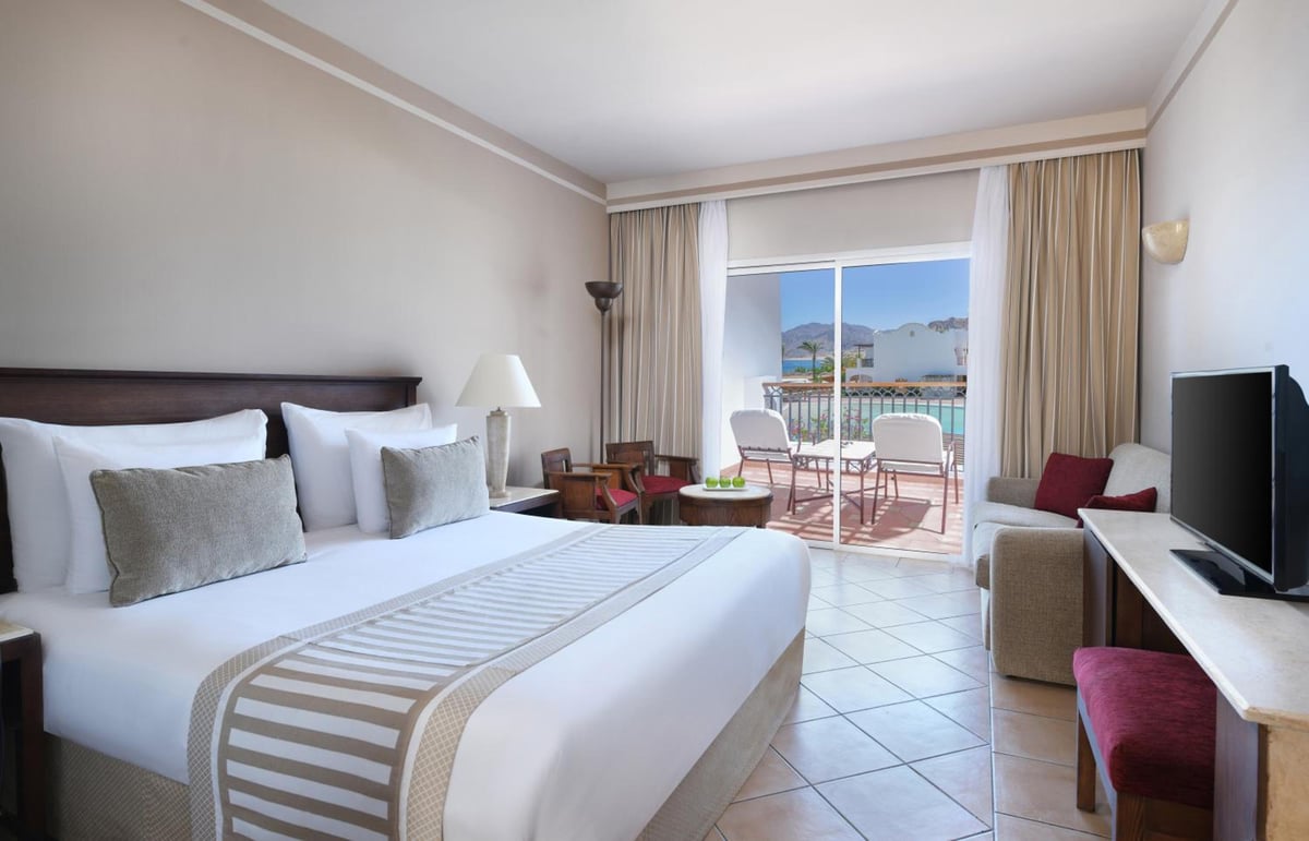 JAZ Dahabeya guest room with a large bed and balcony seating.