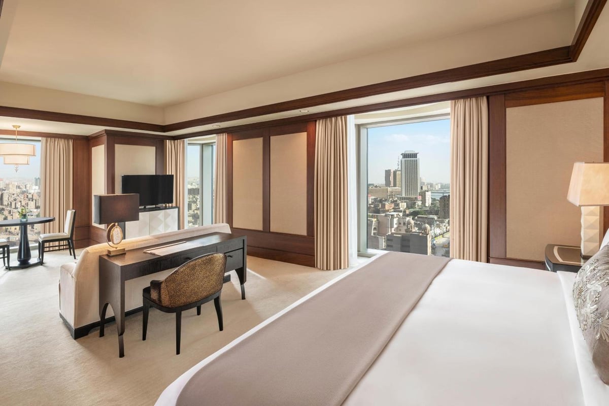 St. Regis Cairo guest room with a large bed and city views through tall windows.