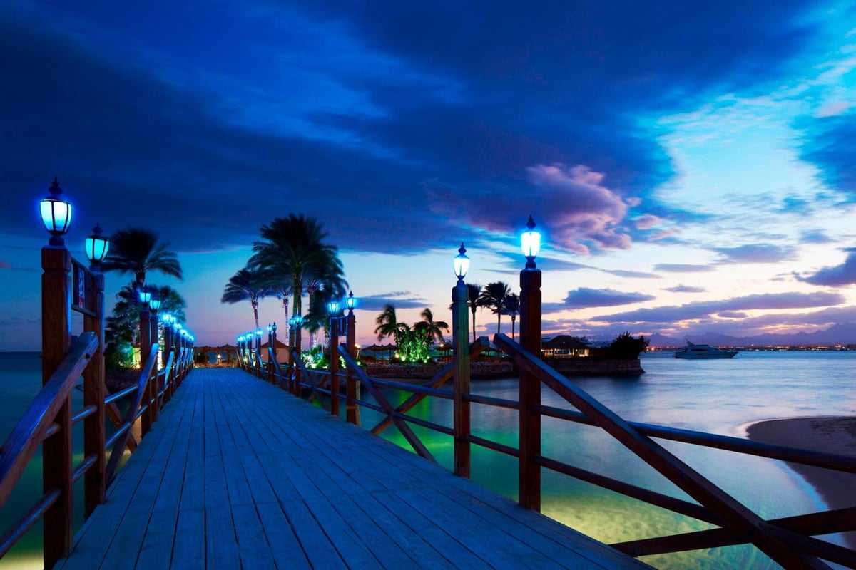 Marriott Hurghada Beach Resort pier with lamp-lit boardwalk and palm-lined shoreline.