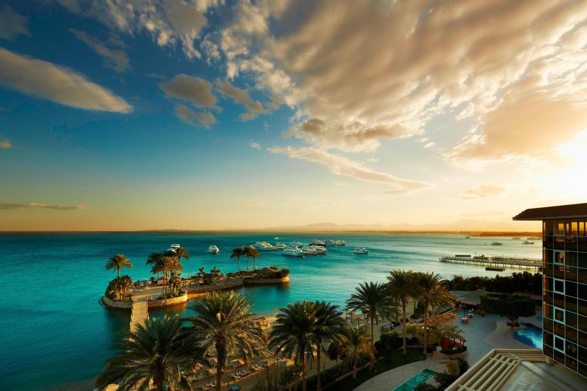 Marriott Hurghada Beach Resort seafront terrace with palm-lined shoreline and moored yachts.