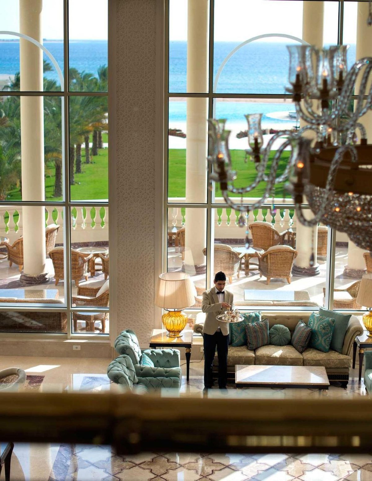 Baron Palace Sahl Hasheesh lobby with teal sofas and tall windows overlooking the sea.