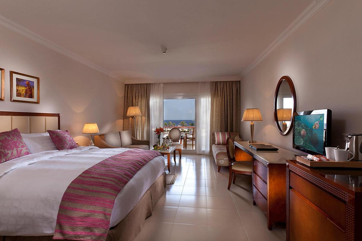 Baron Palace Sahl Hasheesh guest bedroom with a large bed and balcony doors.