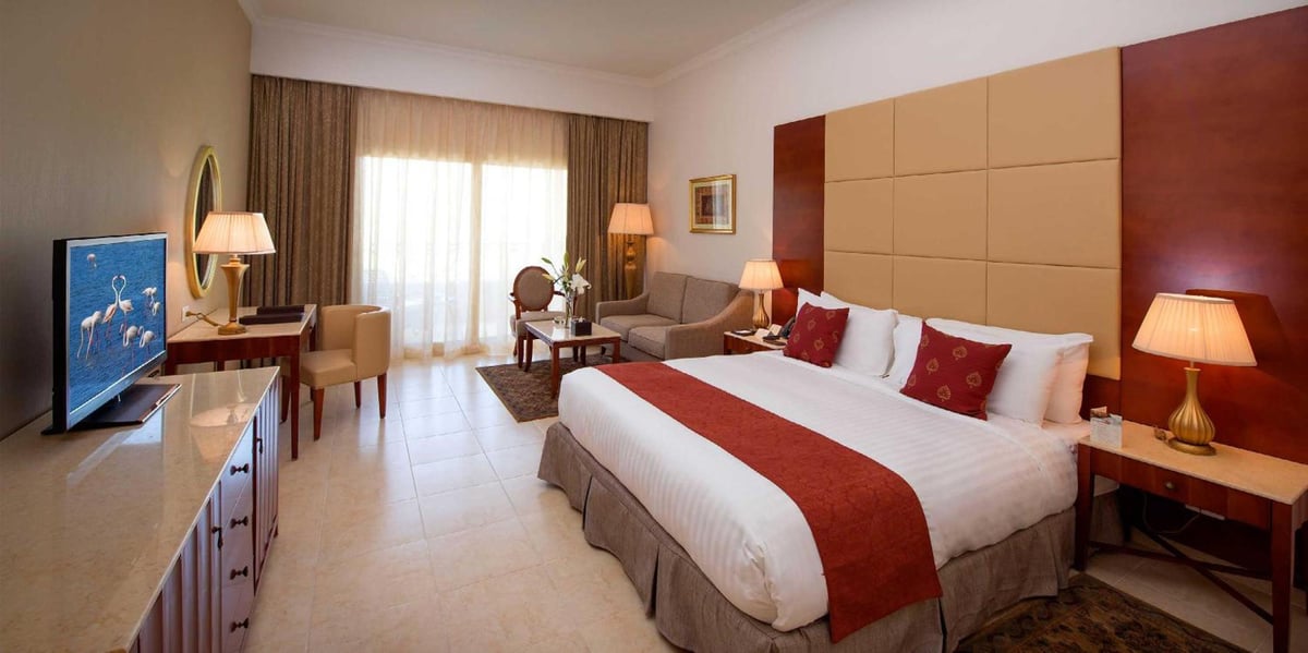 Baron Palace Sahl Hasheesh bedroom with a large bed and curtained glass doors.