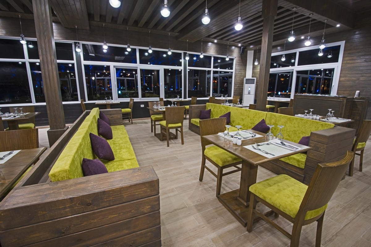 Sunrise Royal Makadi Resort restaurant with wooden tables and green upholstered seating.