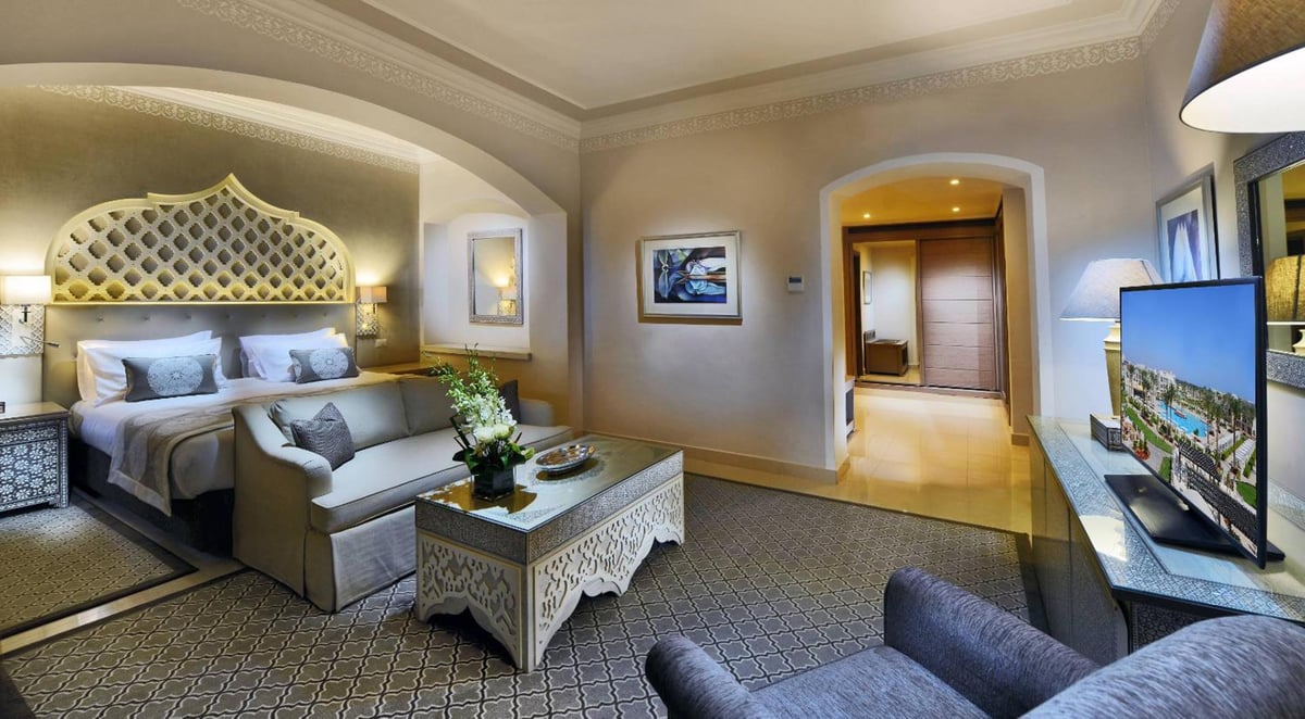 Steigenberger Alcazar guest room with an ornate headboard and a sitting area.