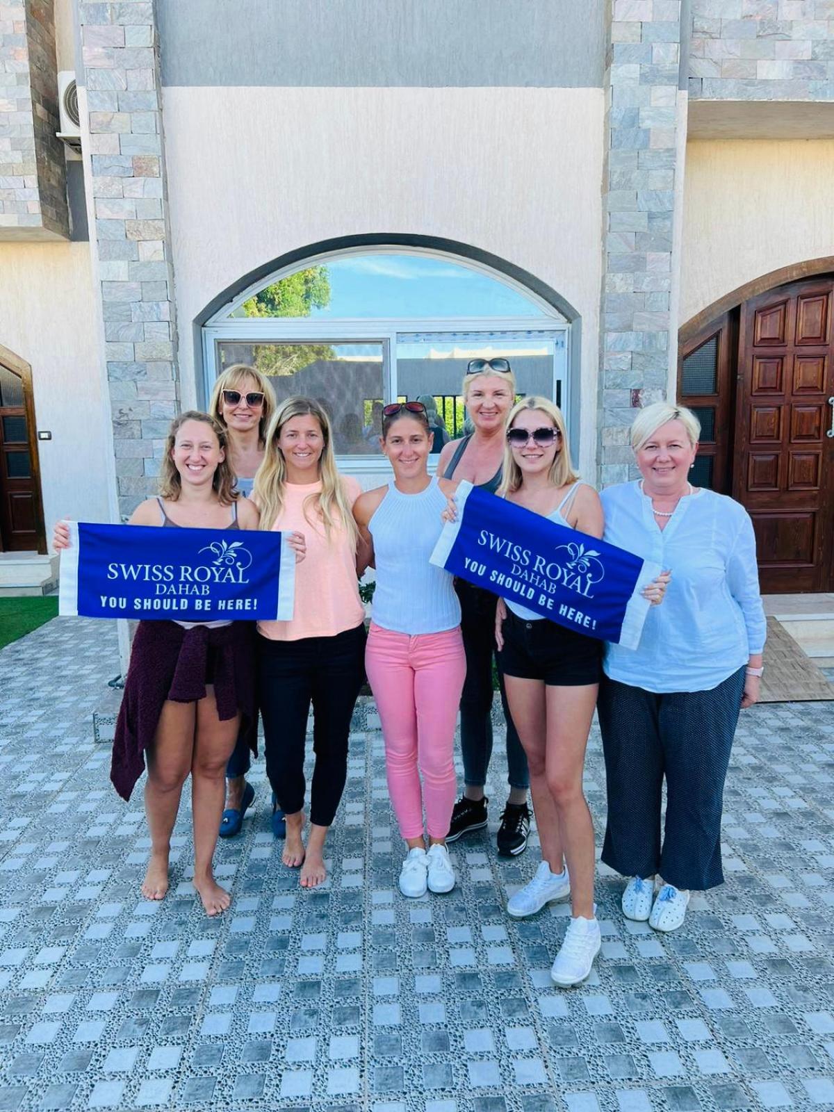 Swiss Royal Dahab hotel entrance with a group holding signs and a stone facade.
