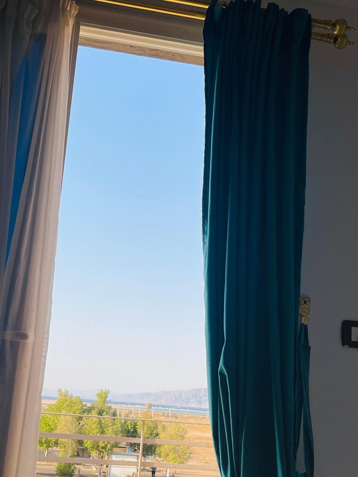 Swiss Royal Dahab room window with blue curtains and a distant landscape.