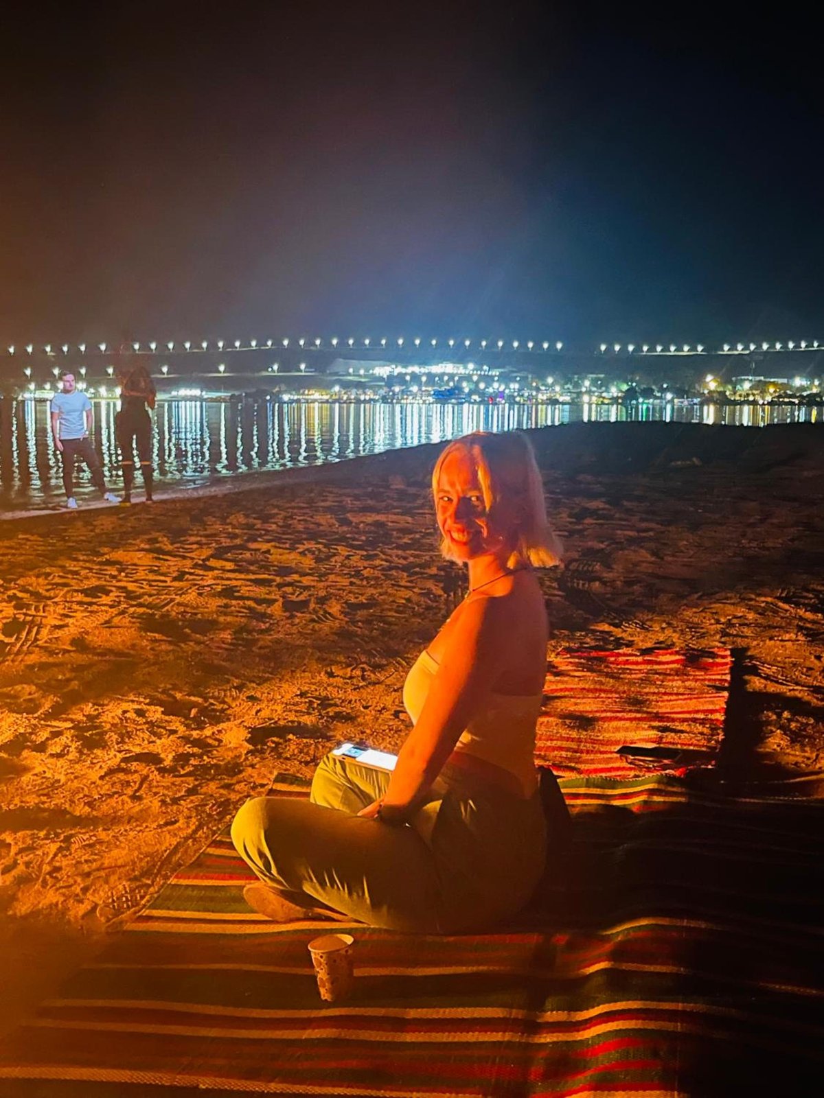Swiss Royal Dahab beach with a seated guest and lights across the water.