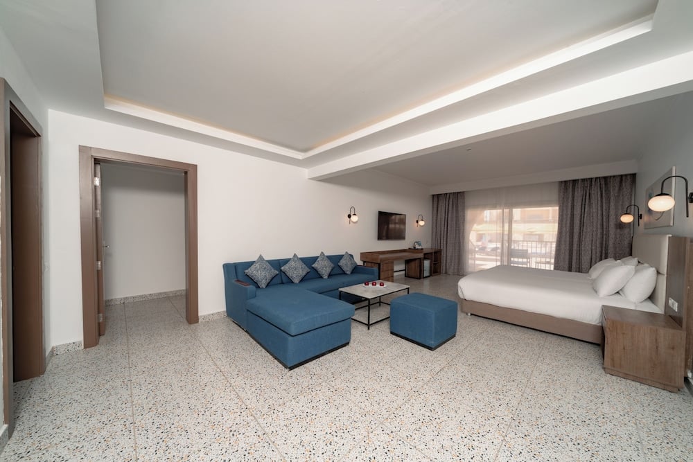 Pickalbatros Vita Resort Portofino guest room with a white bed and blue sofa.
