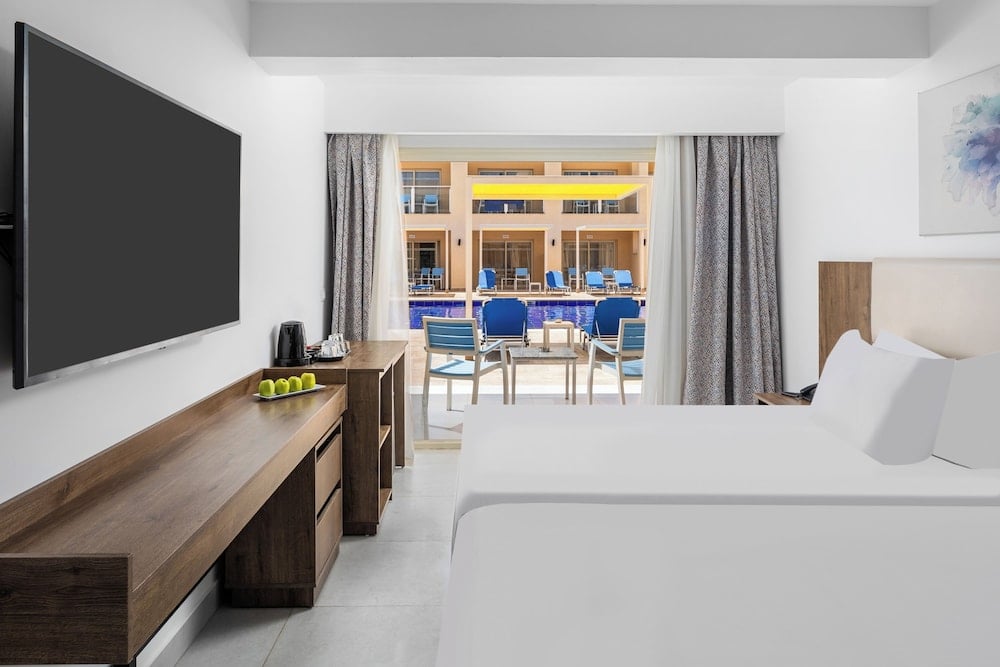 Pickalbatros Vita Resort Portofino bedroom with a white bed and sliding glass doors.