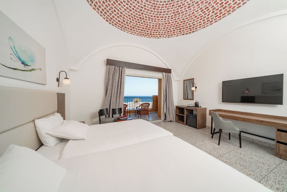 Pickalbatros Vita Resort Portofino guest room with a white bed and balcony doors.