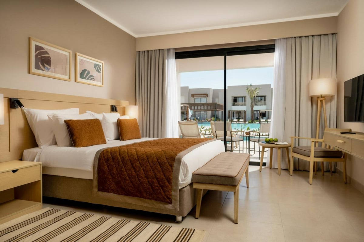 JAZ Elite Amara bedroom with a king bed and glass doors overlooking a pool.