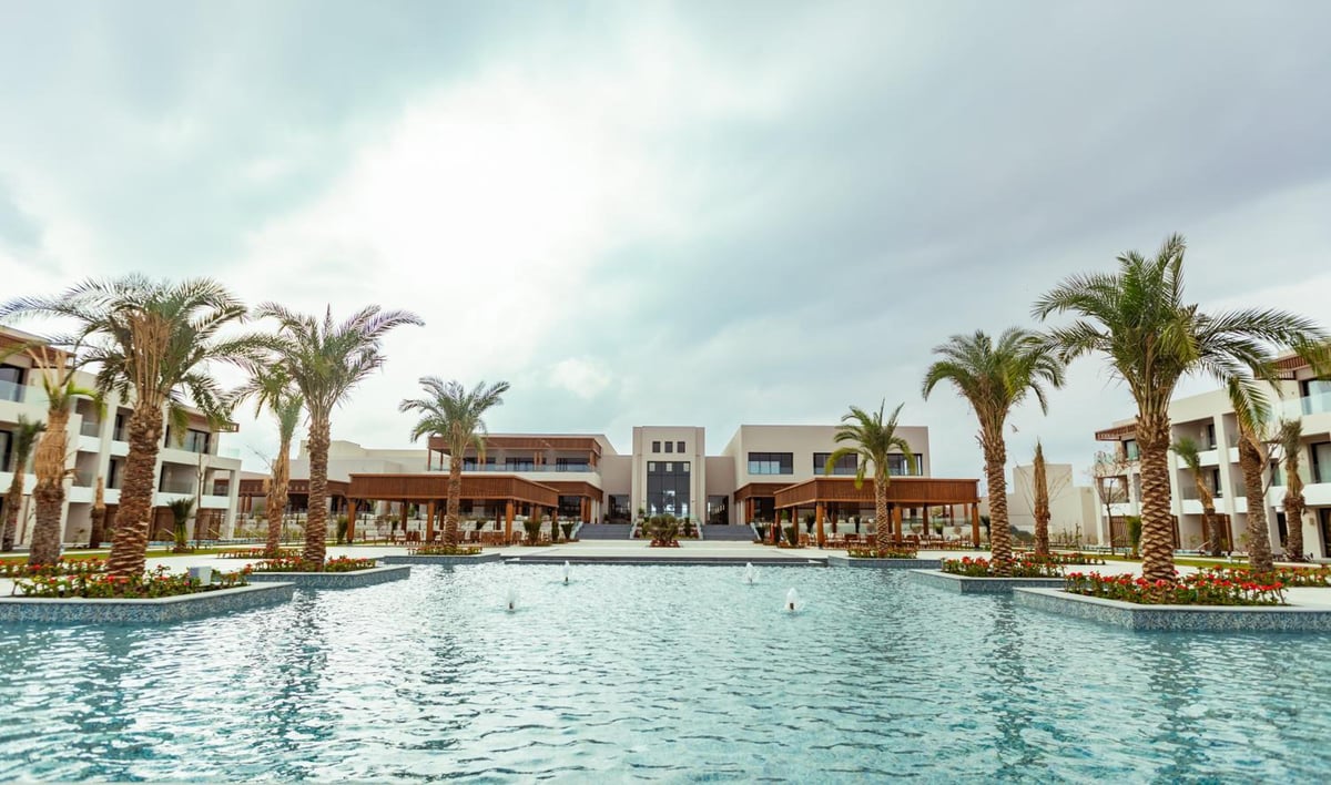 JAZ Elite Amara pool with palm trees and surrounding hotel buildings.