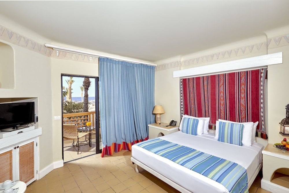 Pickalbatros Sands Port Ghalib bedroom with striped bedding and red curtains.