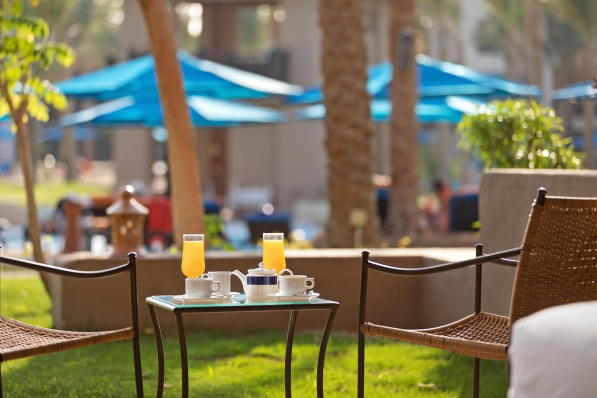 Pickalbatros Sands Port Ghalib garden seating with wicker chairs and blue umbrellas.
