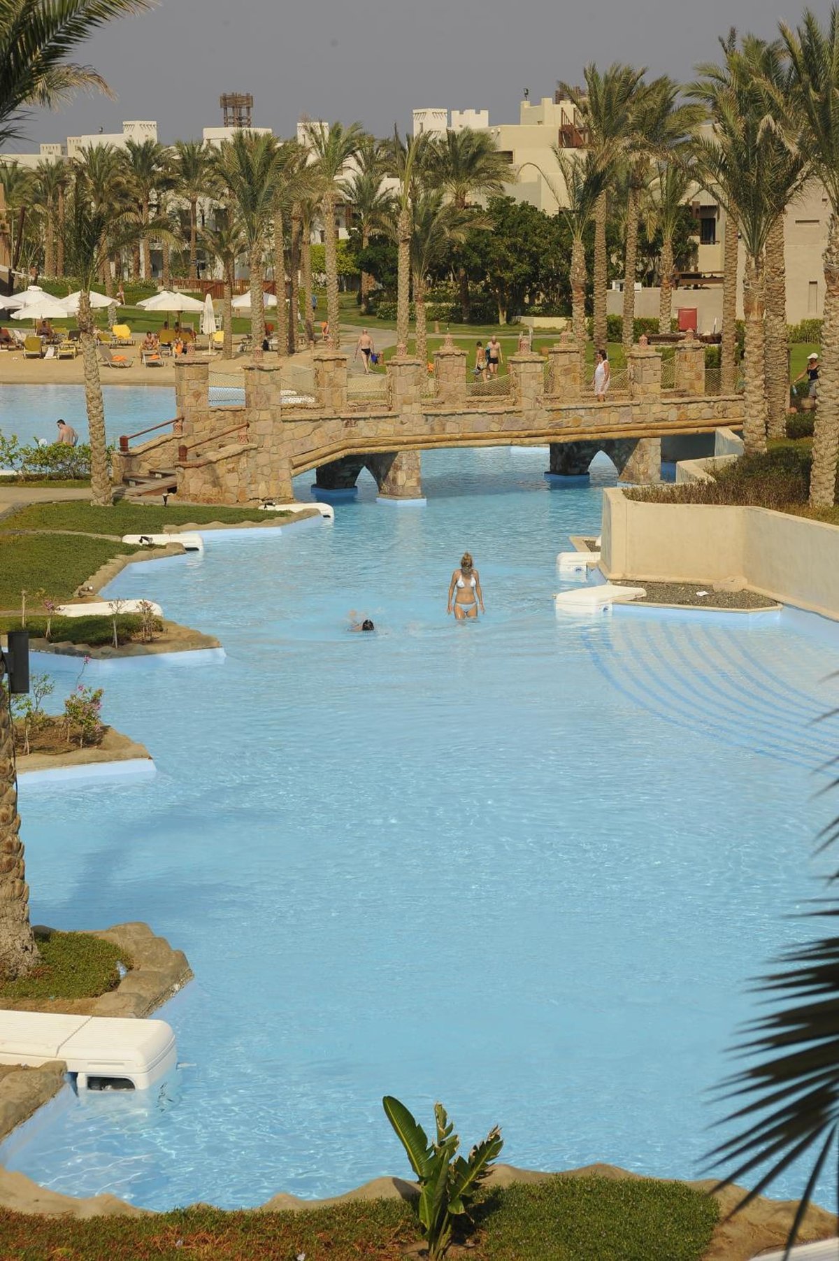 Pickalbatros Sands Port Ghalib resort pool with a stone bridge and palm trees.
