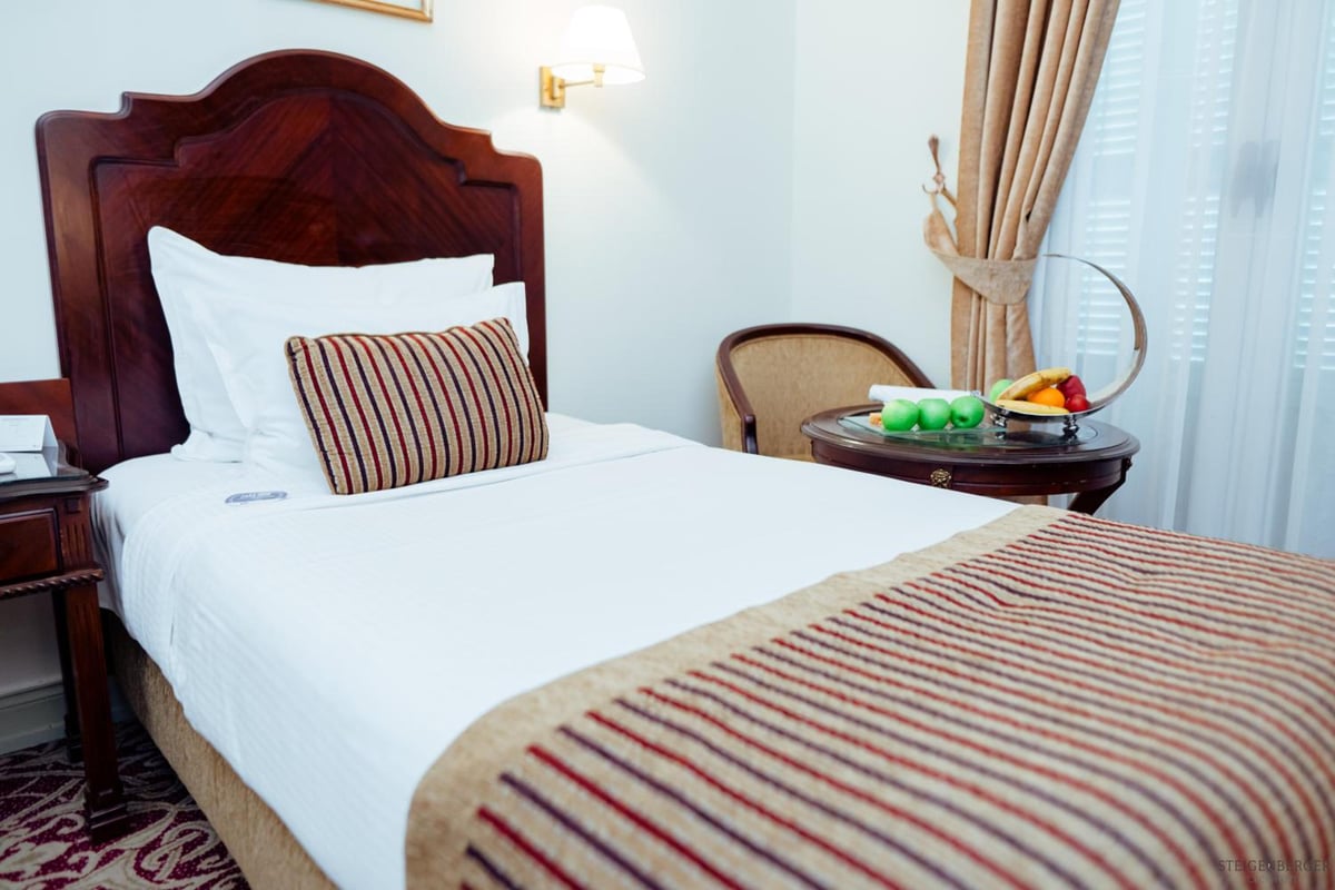 Steigenberger Cecil Hotel Alexandria guest room with a carved wood headboard and striped bedding.