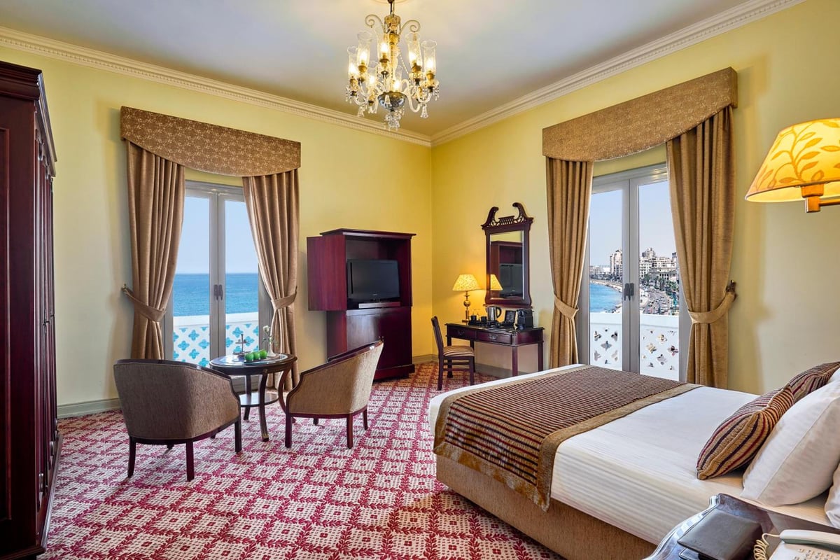 Steigenberger Cecil Hotel Alexandria guest room with patterned carpet and balcony doors overlooking the water.