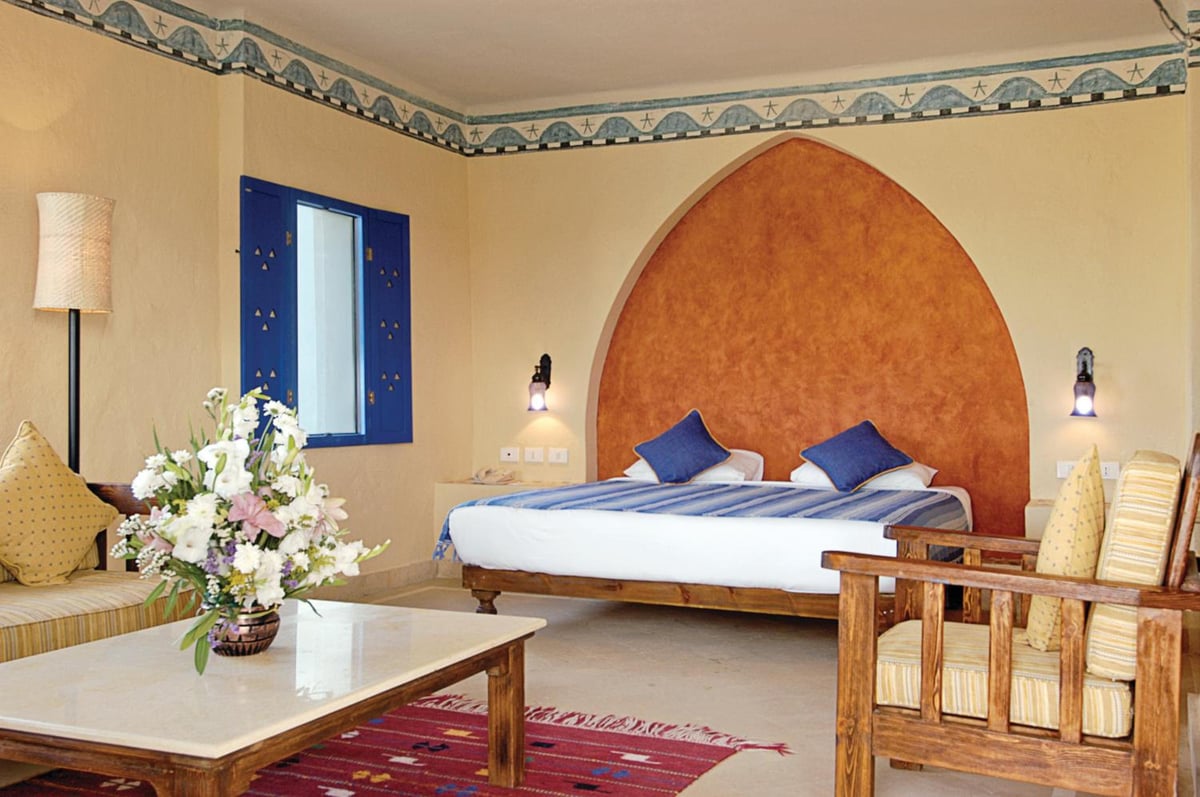 Marina Lodge at Port Ghalib bedroom with an arched terracotta wall and wooden seating.