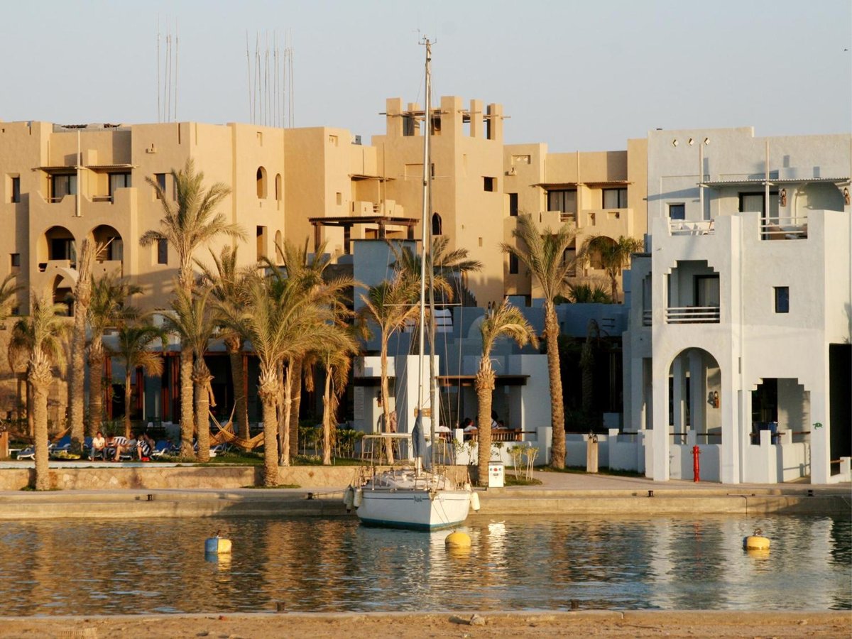 Marina Lodge at Port Ghalib waterfront with moored boats and palm-lined buildings.
