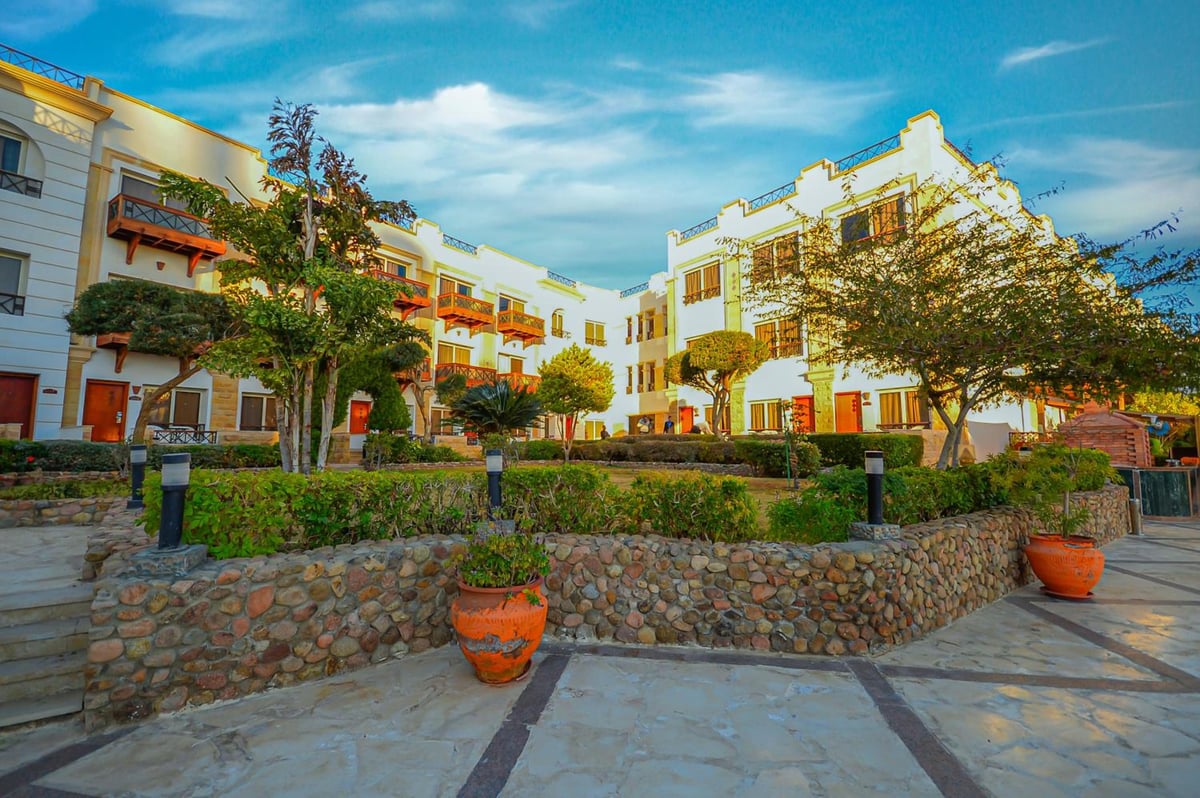 Falcon Naama Star Hotel courtyard with stone garden walls and trees.
