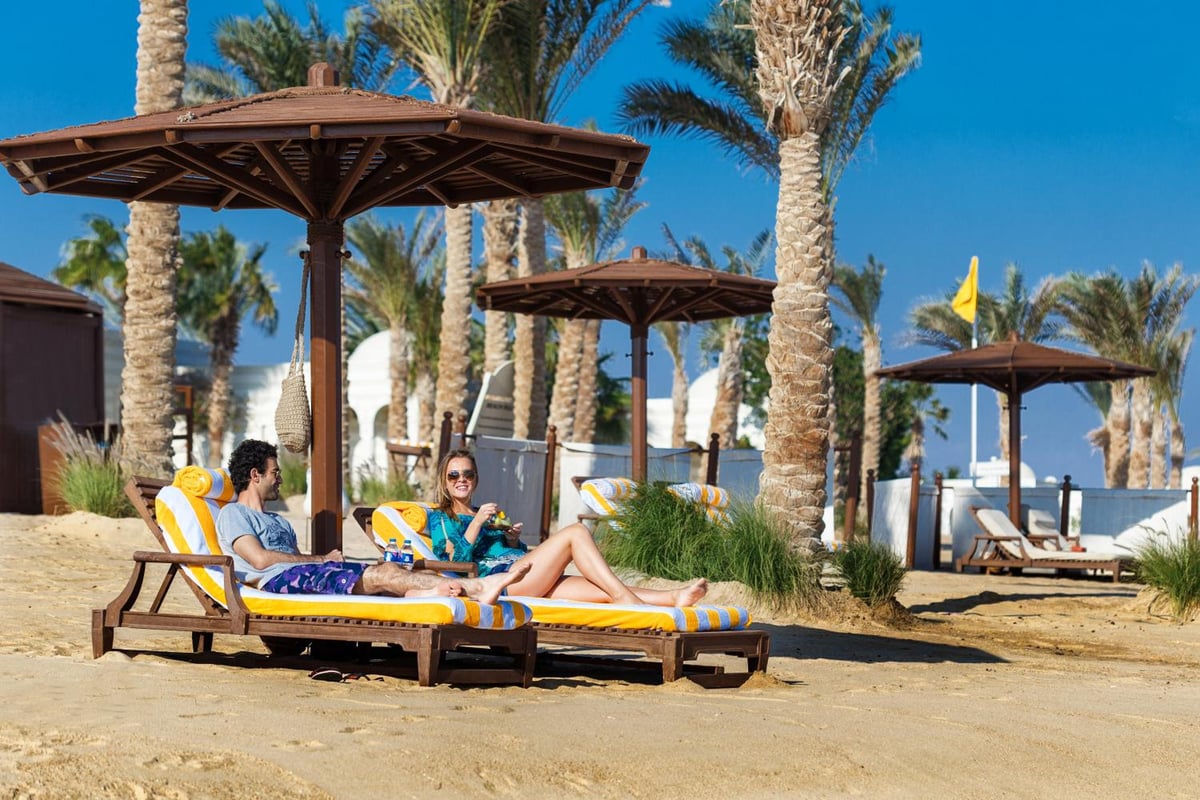 The Oberoi Sahl Hasheesh beach with shaded lounge chairs and palm trees.