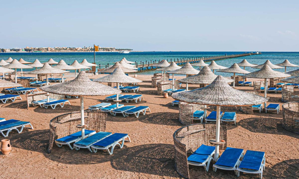 Stella Beach Resort & Spa Makadi Bay beach with thatched parasols and blue sun loungers.