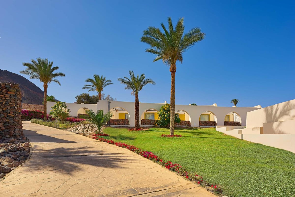 Retac Qunay Dahab Resort & Spa garden path with palm trees and white arched buildings.