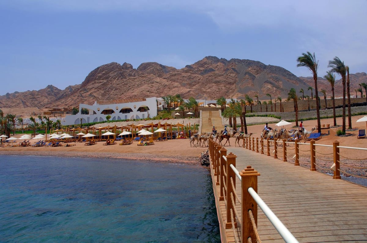 Retac Qunay Dahab Resort & Spa pier with wooden railings and mountains behind the beach.