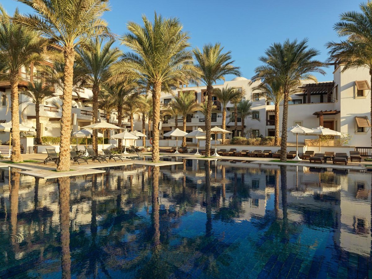 Ancient Sands Golf Resort pool with palm trees and hotel buildings.