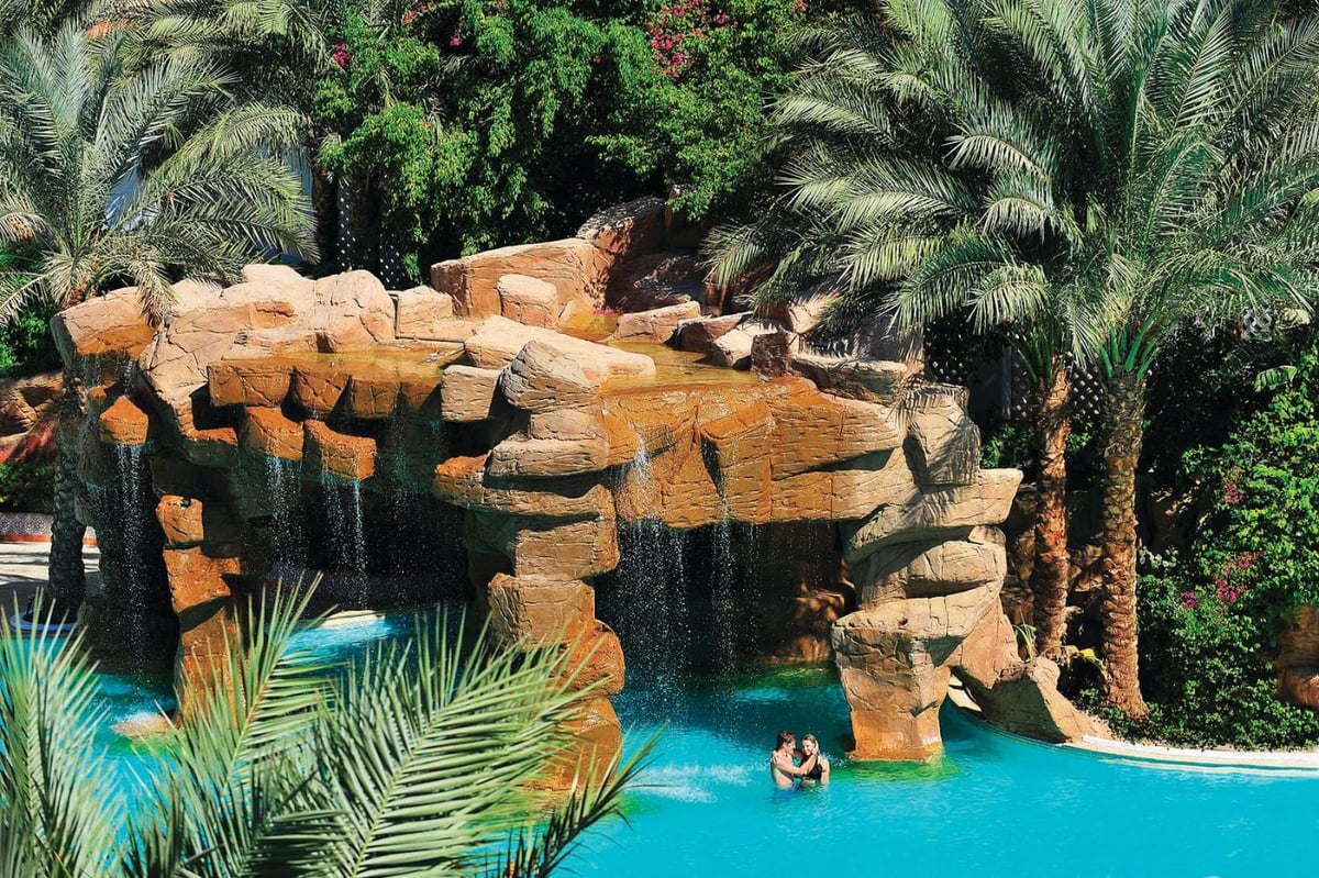 Baron Palms Resort (Adults Only) pool with a rock waterfall and palm trees.