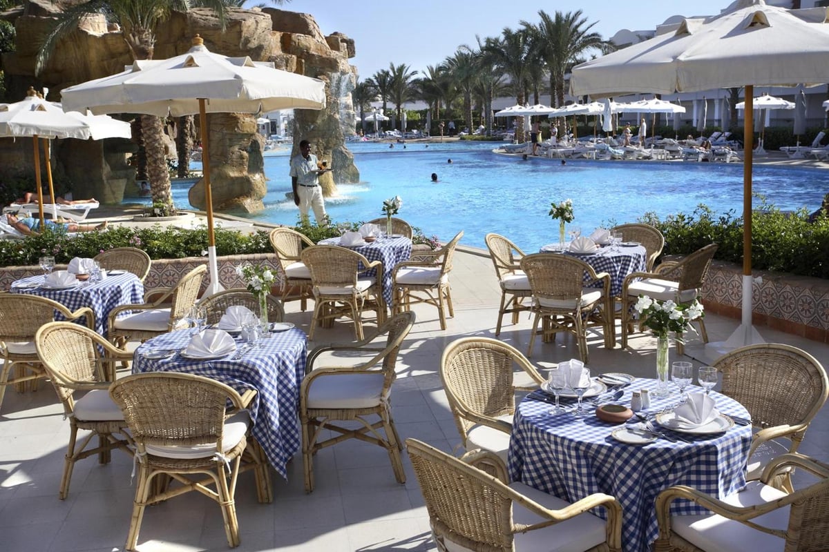 Baron Palms Resort (Adults Only) poolside dining terrace with blue-check tablecloths and white umbrellas.