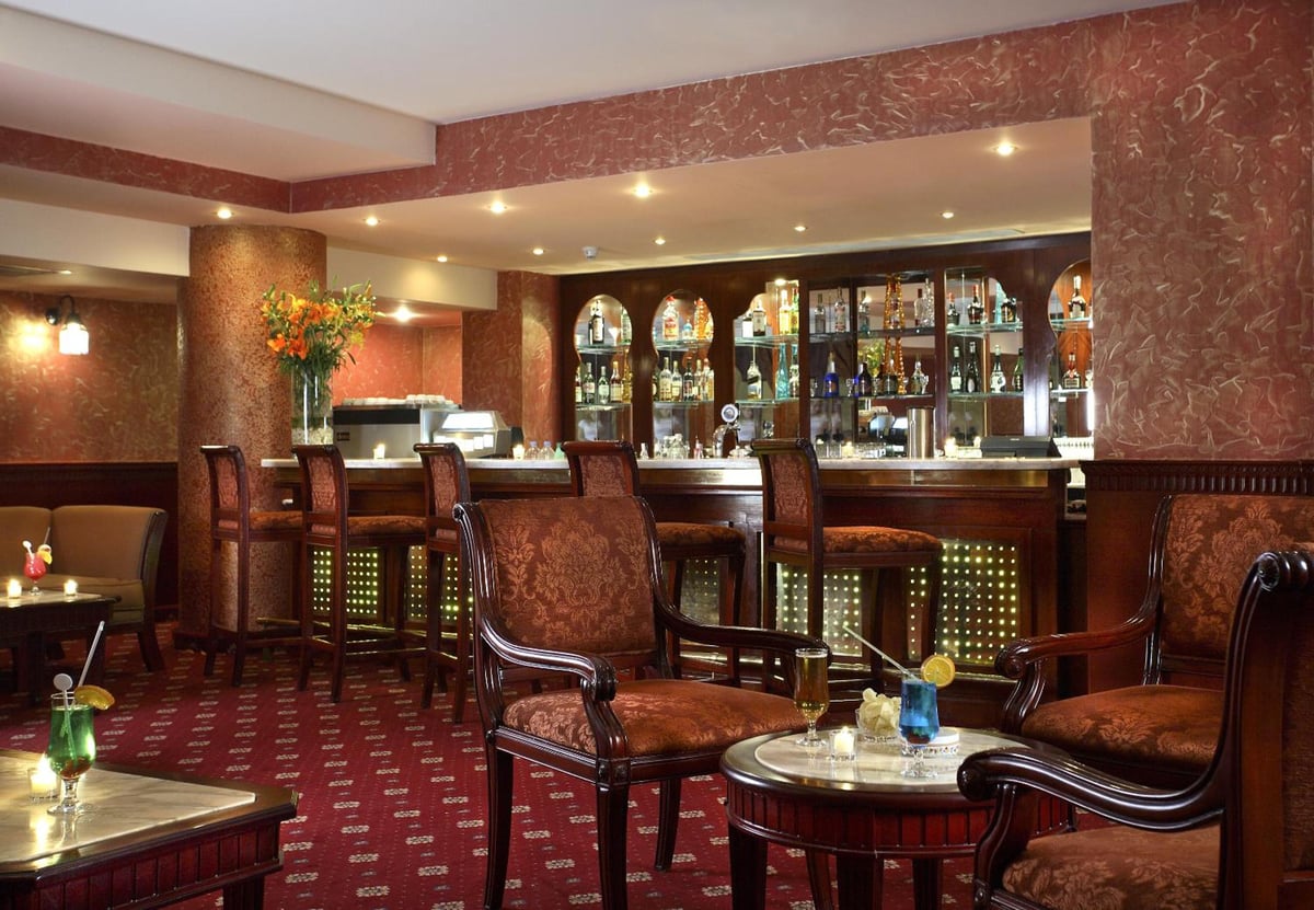 Baron Palms Resort (Adults Only) lounge bar with a wooden counter and upholstered chairs.
