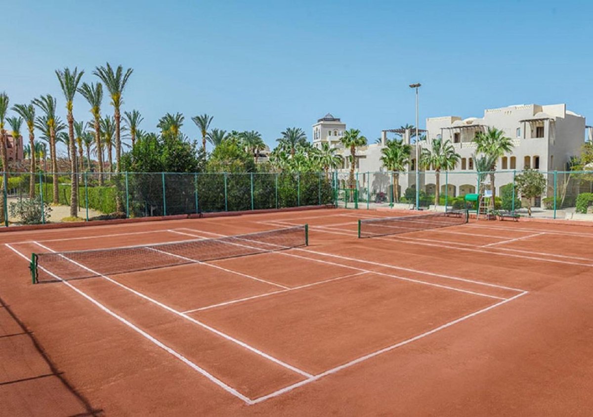 Iberotel Makadi Beach tennis court with terracotta courts and surrounding palm trees.