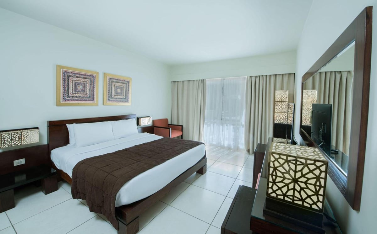 Reef Oasis Beach Aqua Park Resort bedroom with a large bed and curtained glass doors.