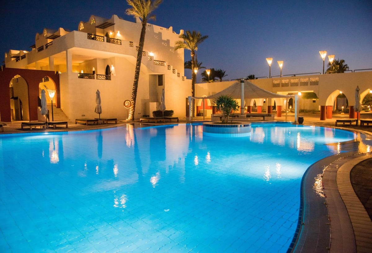 Reef Oasis Beach Aqua Park Resort pool with blue water and illuminated buildings.