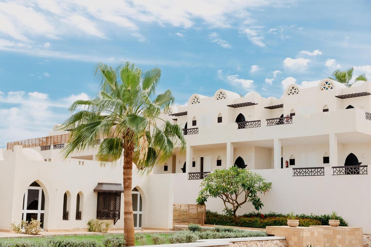 Reef Oasis Beach Aqua Park Resort exterior with arched windows and a palm tree.