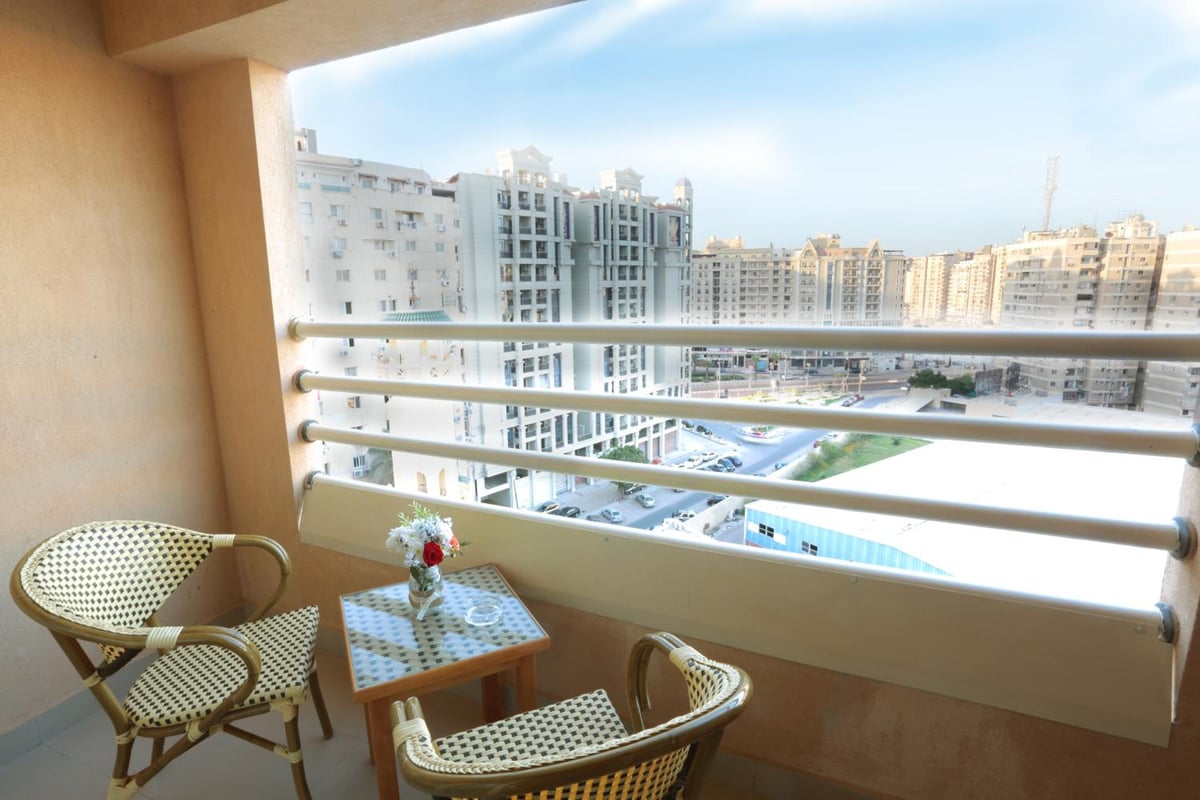The Grand Plaza Hotel Smouha balcony with wicker chairs and city buildings.