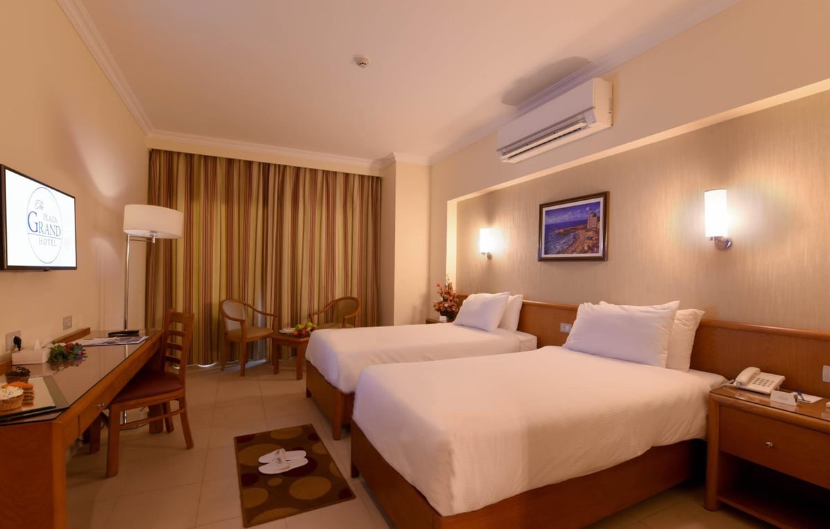 The Grand Plaza Hotel Smouha guest room with twin beds and striped curtains.