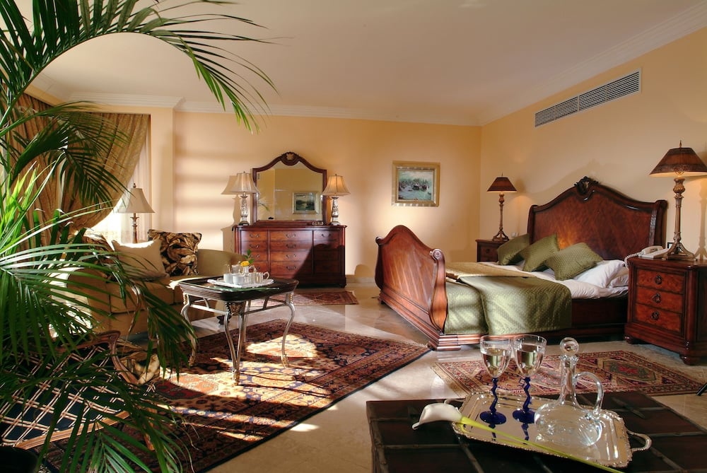 Royal Savoy Sharm El Sheikh bedroom with a carved wooden bed and a sitting area.