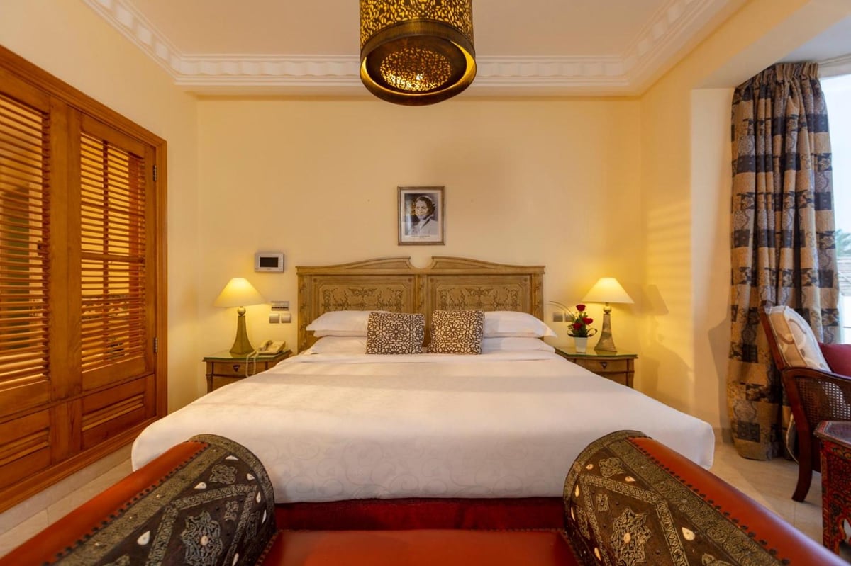Royal Savoy Sharm El Sheikh bedroom with a carved wooden headboard and shuttered windows.