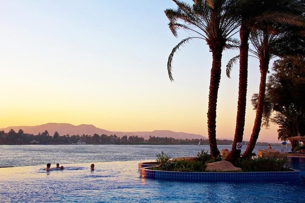 Jolie Ville Hotel & Spa Kings Island Luxor pool with palm trees and a river view.