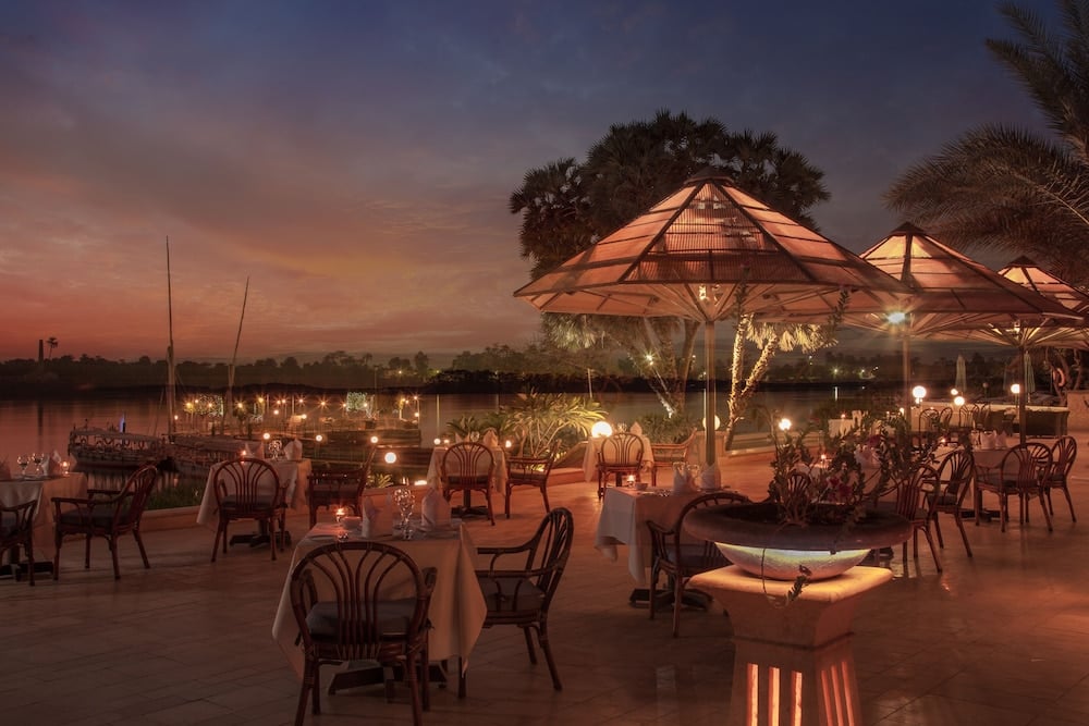 Jolie Ville Hotel & Spa Kings Island Luxor outdoor dining terrace with round tables and illuminated parasols.